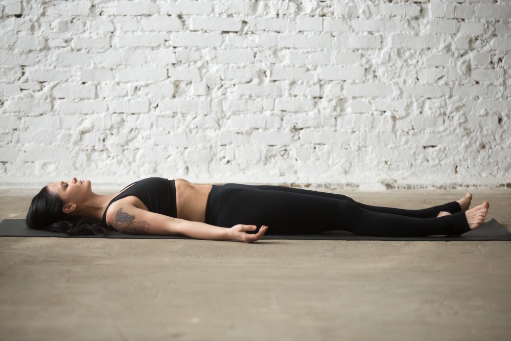 Femme qui est en train de faire la posture du cadavre en yoga